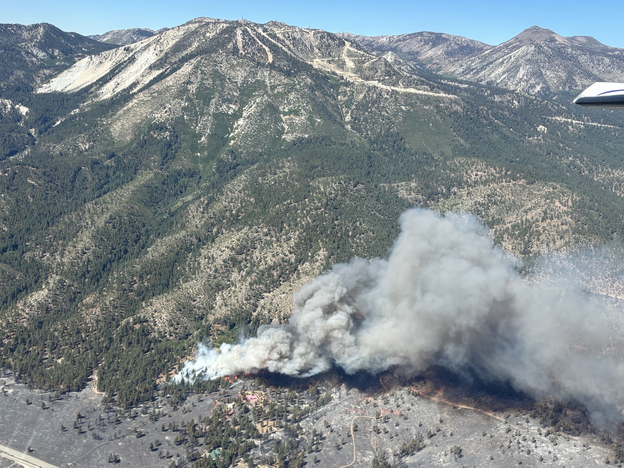 Photo of a mountain range and a wildfire at the base of the mountain.