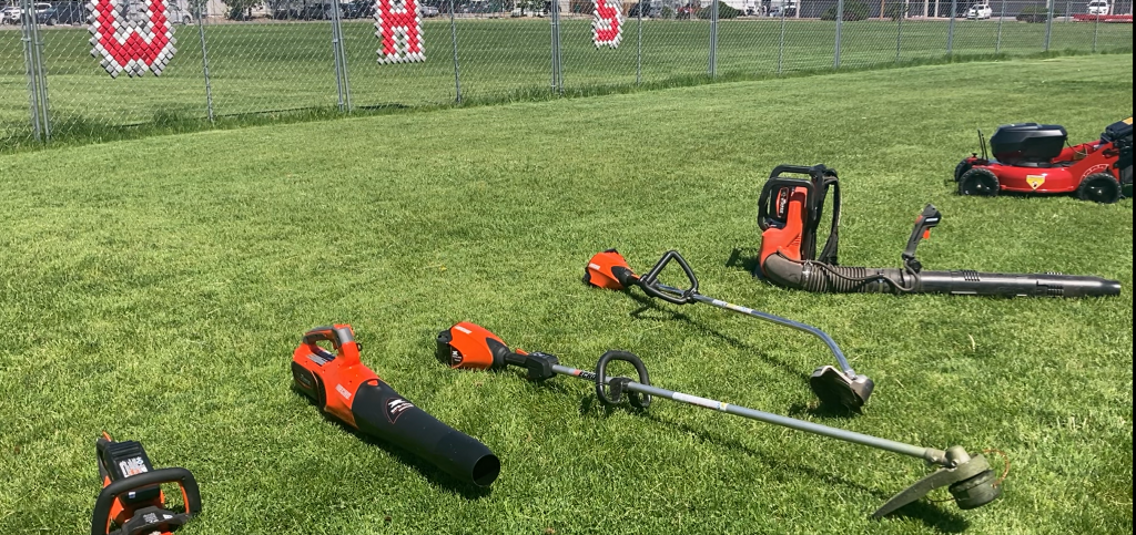 A variety of electric lawn and garden equipment in a row on grass.