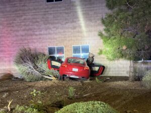 A red car CRASHED INTO THE SIDE OF A BRICK BUILDING WITH THE DOORS OPEN
