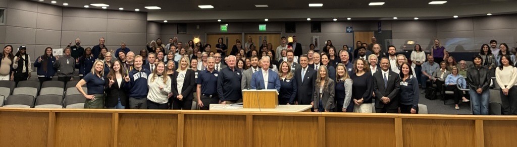 panorama photo of a large group of people in the Washoe County chambers with UNR President Sandoval and Washoe County Commissioners